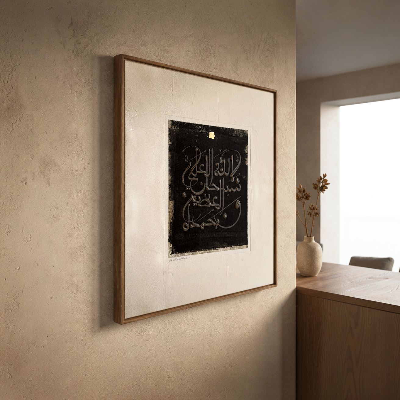 Framed artwork with calligraphy on a beige wall in a room with a window by artist Helen Abbas.